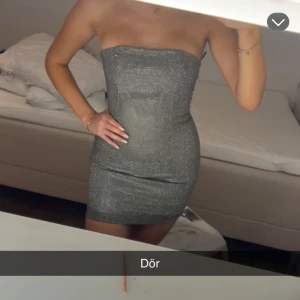 Glittrig tubklänning i silver - Säljer en superfin glittrig tubklänning i silver. Klänningen är tight och kort, perfekt för dig som vill sticka ut. Den har inga axelband och sitter snyggt på kroppen. Perfekt för festkvällar när du vill glänsa lite extra! Har aldrig använt den