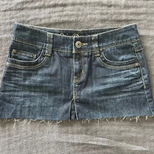 Lågmidjad jeanskjol  - Superkort lågmidjad jeanskjol i klassisk blå denim. Kjolen har fransiga kanter och femficksmodell med knapp och dragkedja framtill. Snygga bakfickor med broderad detalj.. Pris går absolut att diskutera, var inte rädd för o fråga något❣️❣️