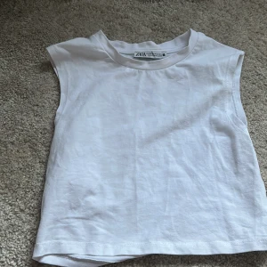 Vit ärmlös linnetopp från Zara - Säljer en enkel och stilren vit ärmlös linnetopp från Zara. Toppen har rund halsringning och är tillverkad i mjuk bomull, perfekt för varma dagar eller som lager under andra plagg.
