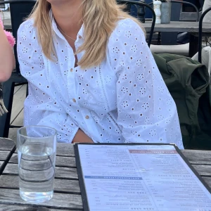 Vit broderad blus med knappar - Säljer en superfin vit blus med broderade blommor och snygga detaljer. Blusen har långa ärmar, knappar framtill och en lätt oversized passform. Perfekt att styla med jeans eller kjol för en fräsch look.