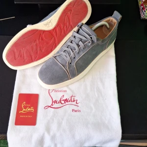 Christian Louboutin Gråblå mocka - Säljer ett par blå sneakers i mocka från Christian Louboutin med vit sula och den klassiska röda undersidan. Skorna har snörning och rund tå, samt diskreta sömdetaljer. Perfekta för dig som gillar stilrena och exklusiva sneakers. Skorna är använda men i bra skick. Priset kan diskuteras.