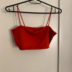Röd croppad linnetopp - Säljer en röd croppad linnetopp med tunna axelband. Perfekt för varma dagar och enkel att matcha med både jeans och kjol. Snygg och stilren design.