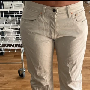 Beige Levis 501 jeansbyxor - Säljer ett par klassiska beige Levis 501 jeansbyxor med raka ben och normal passform. Byxorna har fem fickor, knappgylf och Levis-lapp bak i midjan. Perfekta för en avslappnad och stilren look. W31L34