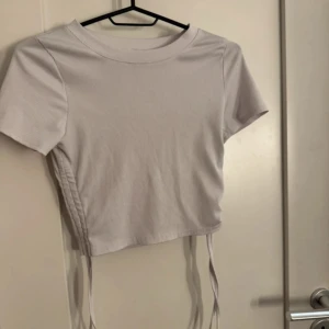 Ljuslila croppad topp med snörning - Trendig ljuslila croppad topp med korta ärmar och snörningsdetalj på sidan. Toppen har en rund halsringning och är tillverkad i ett ribbat material som ger en snygg passform.