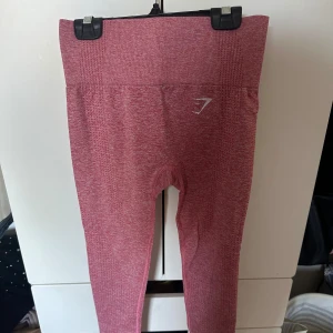 Rosa seamless leggings från Gymshark - Säljer ett par rosa seamless leggings från Gymshark med hög midja och diskret logga på låret. Stretchigt material som sitter tight och bekvämt, perfekt för träning eller gym. Snygg ribbad struktur och figurnära passform.