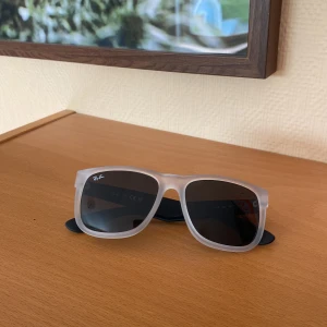 Ray-Ban Justin solglasögon grå/svarta - Snygga Ray-Ban solglasögon med frostade, transparenta bågar framtill och svarta skalmar. Klassisk fyrkantig form och mörka glas. Perfekt accessoar för soliga dagar. Passar dig som vill ha still nu inför sommaren! Knappt använda och har haft dom i nästan ett år. Säljer dom på grund av att jag inte använder dessa.