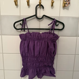 Lila volangtopp från Gina Tricot  - Superfin lila topp från Gina Tricot med volangdetaljer och smockad midja. Axelbanden är justerbara med knyt och toppen har en söt, rynkad design. 💜