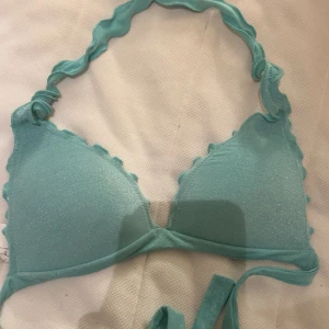 Turkos bikiniöverdel med vågig kant - Säljer en turkos bikiniöverdel med glittrigt tyg och vågiga kanter. Bikinin har knyt i nacken och baktill, vilket gör den justerbar. Helt oanvänd från calzedpnia!! Finns inte på hemsidan längre  