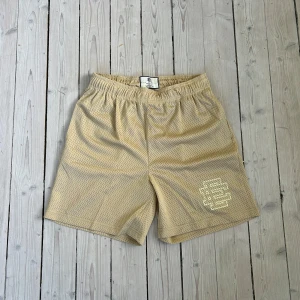 Beige meshshorts från Eric Emanuel - Säljer ett par beige meshshorts från Eric Emanuel med elastisk midja och logga på vänster ben. Shortsen har sportig känsla och är perfekta för varma dagar eller träning.