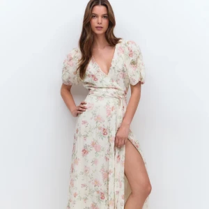 Blommig långklänning med puffärm och slits - Romantisk långklänning i ljusa toner med blommigt mönster. Klänningen har v-ringning, puffärmar och en markerad midja med knytband. Slits framtill ger en extra touch. Perfekt för sommarens alla tillfällen.