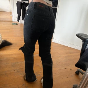 Svarta slitna jeansbyxor - Svarta jeansbyxor med stora slitningar över knäna och slits nere vid innersidan av foten. Jätte sköna och lågmidjade. Skulle säga att dom ligger mitt emellan bootcut och raka.