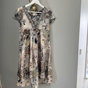 Mönstrad klänning från Odd Molly - Supersöt klänning från Odd Molly med vackert paisleymönster i beige, svart, grått och inslag av orange. Klänningen har korta ärmar, v-ringning och är tillverkad i mjuk viskosblandning. Perfekt för vår och sommar!