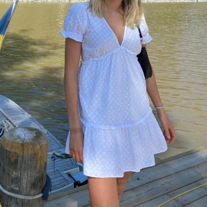 Vit kortklänning med broderade detaljer från Zara - Superfin vit kortklänning från Zara med broderade detaljer och lätt volang nertill. Klänningen har v-ringning, puffärmar och är tillverkad i bomull