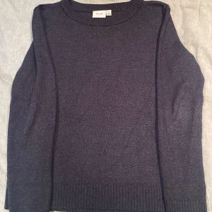 Mörkblå stickad tröja från Vila - Mysig mörkblå stickad tröja från Vila med rund halsringning och långa ärmar. Tröjan har ribbade muddar vid ärmslut och nederkant, perfekt för kyligare dagar.