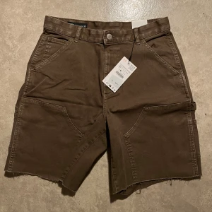 Bruna cargoshorts från Zara - Säljer ett par bruna cargoshorts från Zara med flera praktiska fickor och råa benslut. Shortsen har normal passform och är tillverkade i ett kraftigt bomullsmaterial. Perfekta för en avslappnad stil.