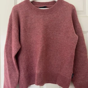 Rosa stickad tröja från Holebrook - Mysig rosa stickad tröja från Holebrook med rund halsringning och långa ärmar. Tröjan har en avslappnad passform och ribbade muddar vid ärmslut och nederkant. Perfekt för kyliga dagar.