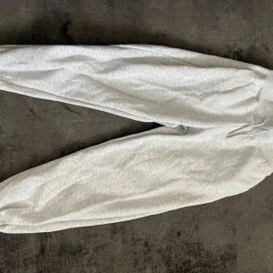 Ljusgrå mjukisbyxor med resår - Säljer ett par ljusgrå mjukisbyxor med resår i midjan och vid bensluten. Byxorna har en avslappnad passform och är perfekta för en chill dag hemma eller till träningen. Klassisk look med dragsko i midjan.