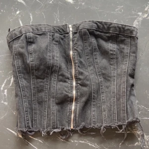 Svart jeanskorsett med dragkedja Zara - Från Zara. Cool svart korsettopp i jeansmaterial med dragkedja framtill och rå, fransig nederkant. Baksidan har smock för extra stretch och passform. Perfekt för en edgy stil.