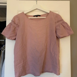 Ljusrosa blus med volangärm från Vero Moda - Säljer en ljusrosa blus från Vero Moda med korta volangärmar och rund halsringning. Blusen är i ett mjukt bomullsmaterial och har en enkel, feminin design med fina rynkdetaljer på ärmarna.