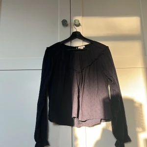  Mörk blå med volang från Gina Tricot - Säljer en svart blus från Gina Tricot med lång ärm och volangdetalj framtill. Blusen har en lätt struktur med små prickar i tyget och rund halsringning. Perfekt för dig som gillar en enkel men ändå söt stil.