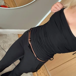 Svart body med rynkade detaljer - Säljer en svart body med rynkade detaljer och smala axelband. Toppen är tight och har en stilren look som passar till många olika outfits. ny med prislapp 