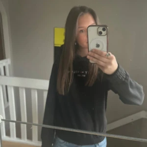 Svart hoodie från Tommy Hilfiger - Säljer en svart hoodie från Tommy Hilfiger med logga och text på bröstet. Klassisk huva och ribbade muddar vid ärmslut och nederkant. Perfekt för en avslappnad stil.