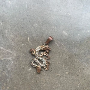 Halsbandshänge y2k - Riktig metall! Snyggt halsbandshänge i form av en drake, dekorerad med glittriga stenar på framsidan. Hänget är i guldtonad metall och har en cool, detaljerad design som sticker ut.