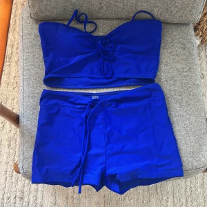 Kornblå bikini med topp och shorts - Den är mörkare blå i verklighet, aldrig använd och absolut inga skador eller sånt. Är i storlek m men passar också som en S.Säljer en kornblå bikini med axelbands-topp och matchande shorts. Toppen har smala axelband och knytdetalj framtill. Shortsen har snörning i midjan. Perfekt för stranden eller poolen! 