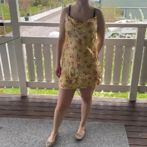 Gul blommig klänning från Zara - Söt gul klänning från Zara med rosa blommönster och tunna axelband. Klänningen har en lätt volang nertill och är kort i modellen. Perfekt för varma dagar och somriga tillfällen.