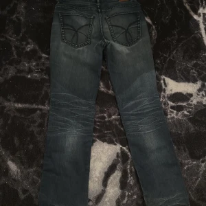 Mörkblå jeans från Calvin Klein Jeans - Säljer ett par mörkblå jeans från Calvin Klein Jeans med snygga slitningar och broderade bakfickor. Modellen är Regular Slim med klassisk femficksdesign och subtila detaljer. Perfekta för dig som gillar stilrena och tidlösa jeans.