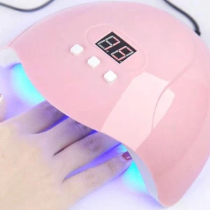 Rosa UV-lampa för naglar - Säljer en rosa UV-lampa för naglar med digital display och tre vita knappar för timerinställning. Perfekt för att härda gel- eller shellacklack. Lampan har en rundad form och lyser blått inuti.