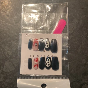 Svarta lösnaglar med Spirited Away-motiv - Säljer ett set med svarta lösnaglar med handmålade motiv inspirerade av Spirited Away, inklusive No-Face och röda detaljer. Paketet innehåller även en rosa nagelfil och självhäftande klisterlappar för enkel applicering.
