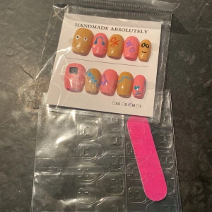 Handgjorda färgglada lösnaglar med motiv - Säljer ett set med handgjorda lösnaglar i rosa och gult med unika motiv och figurer. Setet innehåller nagelfil och klisterlappar för enkel applicering. Perfekt för dig som vill ha en kreativ och färgglad nagelstil.
