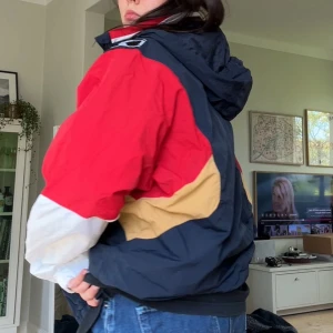 Flerfärgad vindjacka med huva från Kappa - Säljer en retroinspirerad vindjacka från Kappa med huva och dragkedja. Jackan är färgblockad i marinblått, rött, vitt och beige med svarta Kappa-loggor längs axlarna. .