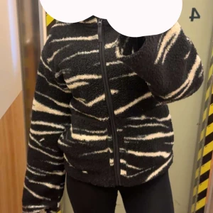 Teddyjacka hm - Mysig teddyjacka i svart med vita zebraränder. Jackan har dragkedja framtill och lång ärm. Perfekt för dig som vill ha en cool och bekväm stil.