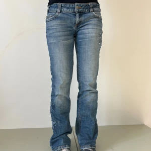 Jeans #31 - Ljusblå jeans med stjärndetaljer - Mått: Midja: 39 cm Innerbenslängd: 77 cm 