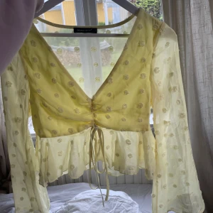 Gul blus - Söt gul blus från double crazy med transparenta långa ärmar, volang nertill och knyt framtill. Blusen har v-ringning och är dekorerad med små blommiga prickar i samma färg för en romantisk look. Den är i storlek S men skulle säga mer XS/S.