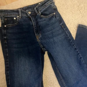 Blå bootcut jeans med hög midja från &Denim - Mörkblå jeans med bootcut-modell och hög midja från &Denim. Klassisk femficksdesign och snygga kontrastsömmar. Perfekta för dig som gillar en tidlös jeansstil med lite utsvängda ben.
