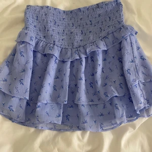 Ljusblå blommig volangkjol från Gina Tricot - Supersöt ljusblå kjol från Gina Tricot med små blommor och flera volanger. Kjolen har smock i midjan och är kort, perfekt för en fräsch look. Tunt och luftigt material som är perfekt nu till sommaren🌸💗