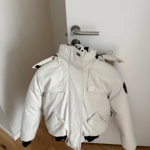 Vit dunjacka med päls från Nobis. Limited edition! - Använd ett fåtal gånger i storlek L men fungerar absolut som M. Nypris: 12 000 kr. Säljer en snygg vit dunjacka från Nobis med avtagbar huva och fuskpäls. Jackan har dragkedja, knappar och flera fickor framtill. Perfekt för kalla dagar med sin höga krage och varma material. Stilsäker och funktionell design.
