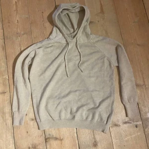 Beige hoodie med huva och dragsko - Säljer en enkel och stilren beige hoodie högjord av 100% merinoull med huva och dragsko. Tröjan har långa ärmar och ribbade muddar vid ärmslut och nederkant. Perfekt för en avslappnad look.