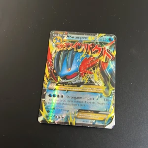 Pokémonkort M Swampert EX - Säljer ett Pokémonkort av typen M Swampert EX med japansk text och färgstark design. Kortet har holografiska effekter och visar Swampert i en dynamisk pose. Baksidan har klassisk blå Pokémon-design med pokéboll i mitten.