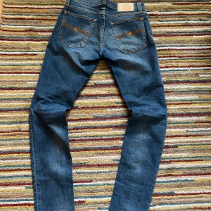  Nudie Jeans - Säljer ett par klassiska blå jeans från Nudie Jeans med snygga kontrastsömmar och broderad bakficka. Modellen har normal passform och raka ben. Aldrig använda. Priset ej hugget i sten, kom med förslag😃