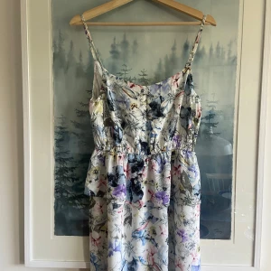 Blommig sommarklänning från Twist & Tango, stl 40 - Söt blommig klänning från Twist & Tango med smala axelband och markerad midja. Klänningen har ett ljust tyg med blommigt mönster i blått, lila och rosa toner. Tillverkad i viskos, perfekt för varma dagar.