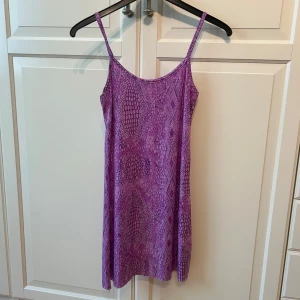 Lila kortklänning med ormmönster från Fashion 100 - Säljer en lila kortklänning med ormmönster från Fashion 100. Klänningen har en figurnära passform i strl s