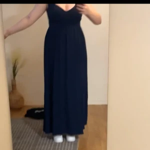 Marinblå långklänning med v-ringning - Säljer en elegant marinblå långklänning med v-ringad hals och breda axelband. Klänningen har en figurnära överdel och faller mjukt från midjan ner till golvet. Perfekt för festliga tillfällen. Väldigt bekväm att röra sig i
