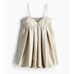 Champagnefärgad kort klänning med tunna axelband - Supersöt kort klänning i champagnefärgat satinliknande material med tunna axelband och markerad byst. Klänningen har en luftig och voluminös kjol som ger en trendig look. Perfekt för sommarens alla tillfällen! Använd en gång och helt slutsåld!💕