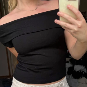Svart offshoulder topp - Säljer en svart offshoulder topp i mjukt bomullsmaterial. Toppen har en bred kant över axlarna och sitter tight mot kroppen. Perfekt för dig som vill ha en stilren och enkel look.