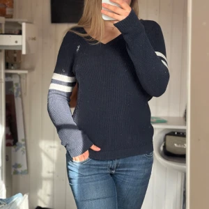 Mörkblå stickad tröja -  Mörkblå ribbad tröja med vita ränder på ärmarna.  V-ringad. Är i storlek 13/14 kids men skulle säga att den är mer S/M. Jag har vanligtvis M och den passar mig. Lite nopprig men går lätt bort med maskin men min maskin har tyvärr gått sönder.
