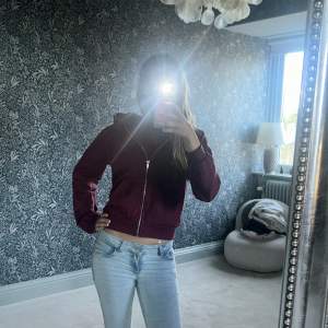 Säljer en vinröd hoodie med dragkedja och huva. Jackan har en croppad passform och är långärmad. Perfekt för dig som gillar en avslappnad stil och vill ha något bekvämt och snyggt.
